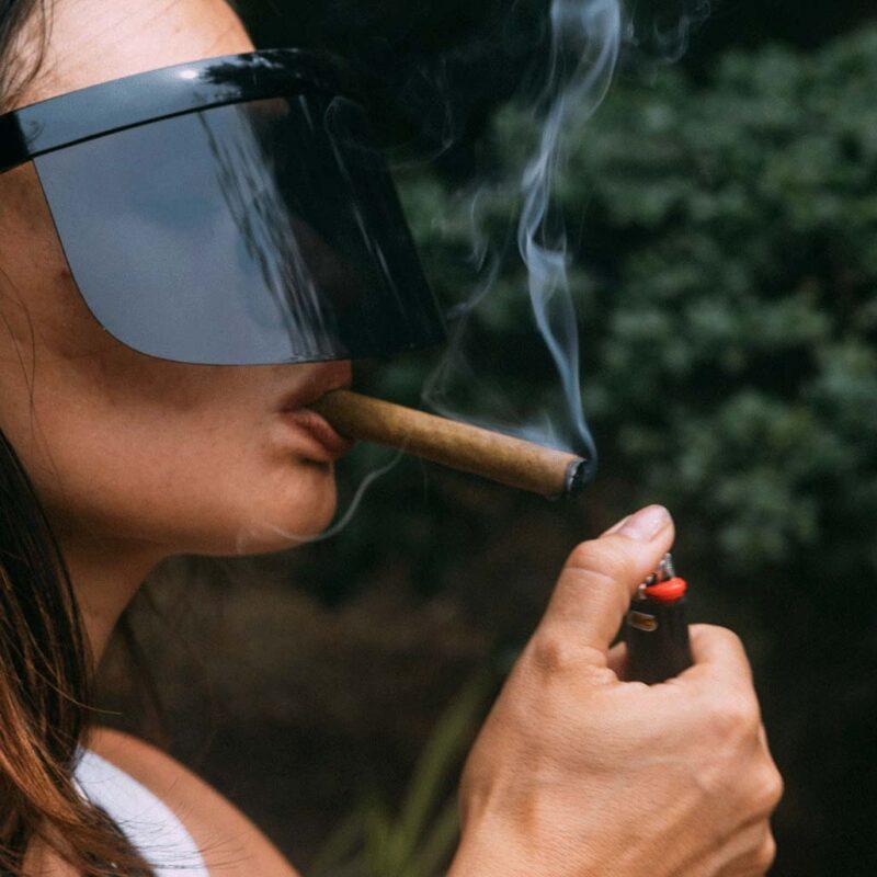 A tanned girl in black sunglasses lights up a blunt weed