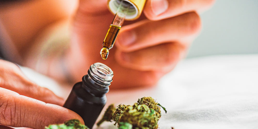 A dropper with a drop of cannabis tincture over a tongue, macro shot.