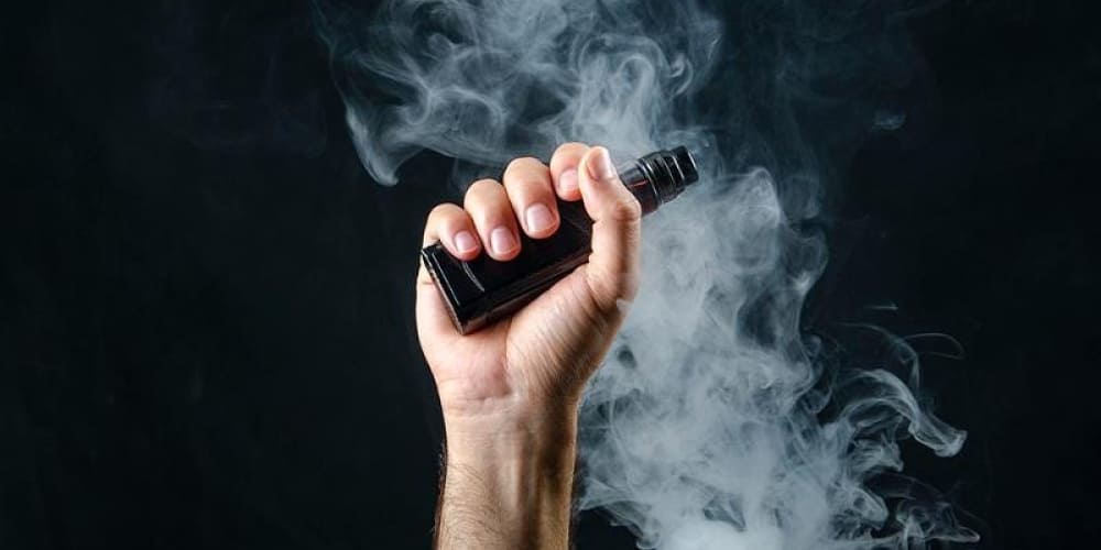 A collection of vaping devices, including pod systems, box mods, and e-liquids, arranged on a modern table.