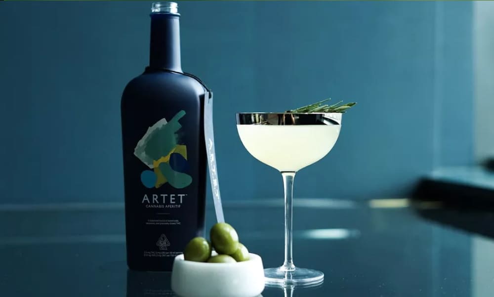 Best 5 THC Drinks A dark, minimalist bottle of Artet Cannabis Aperitif standing next to a sophisticated cocktail in a coupe glass, garnished with a rosemary sprig. A small white bowl of olives is also present.