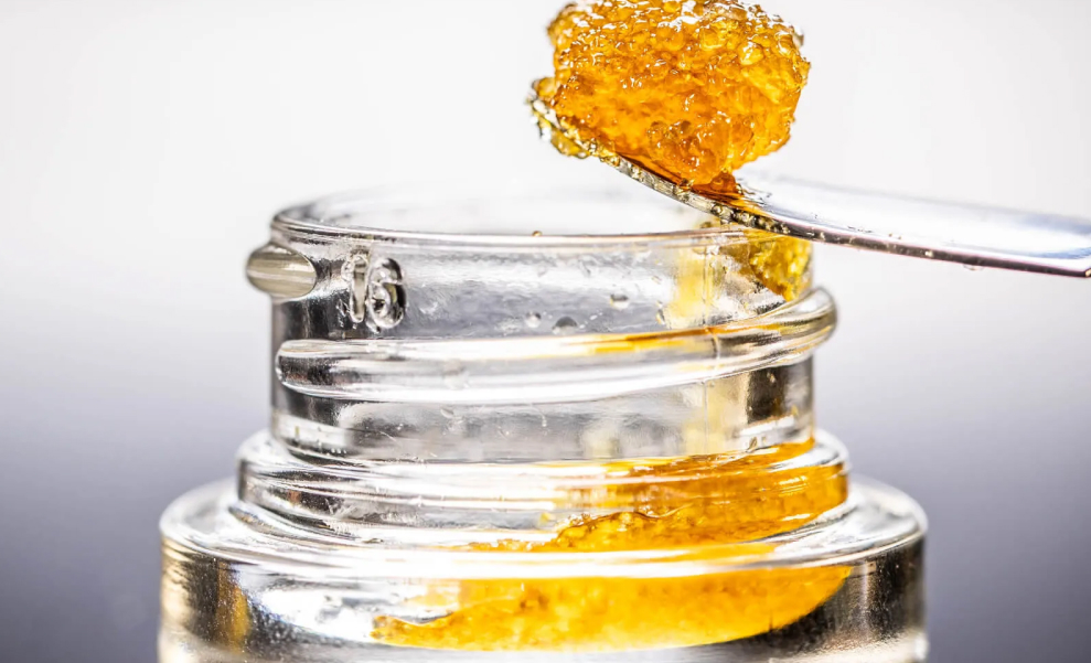 What Is Live Resin Sugar? A dab tool scooping a portion of Live Resin Sugar from a container, highlighting its sticky, granular consistency.