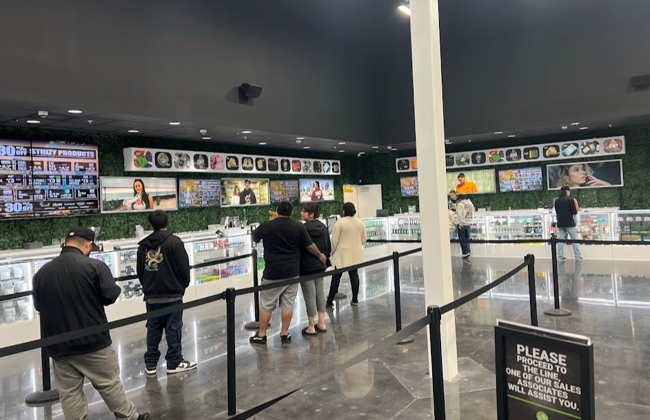 Customers standing in a socially distanced line inside a large cannabis retail store.