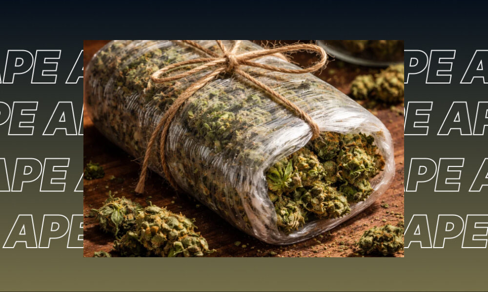 Large bundle of green cannabis flower buds wrapped in clear plastic on a wooden surface.