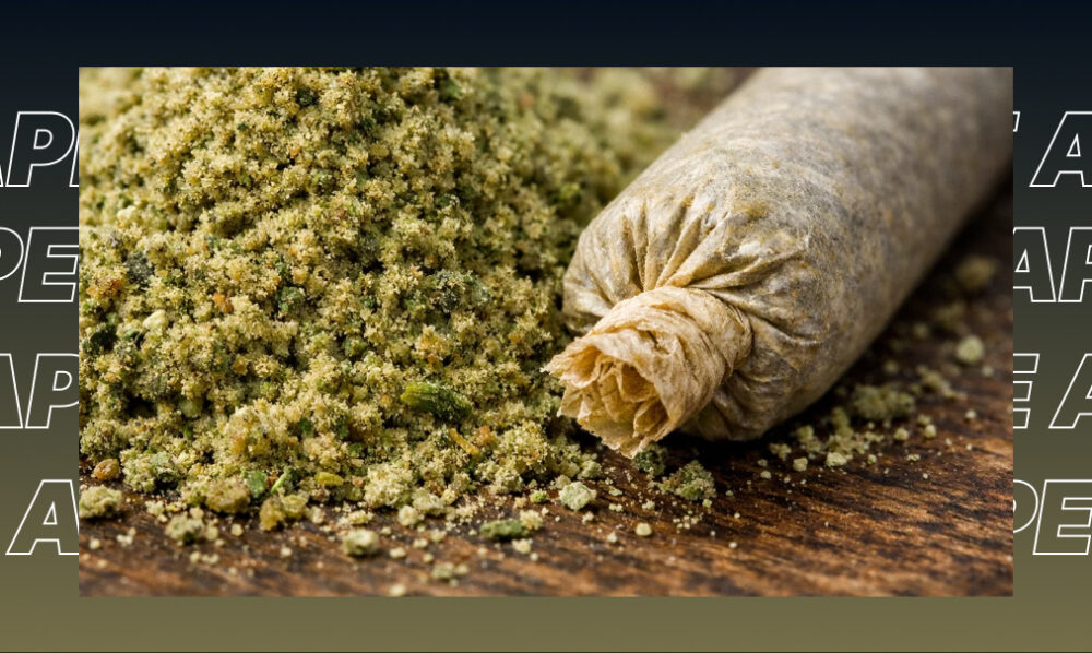 A pile of ground cannabis flower next to a perfectly hand-rolled joint on a wooden table.