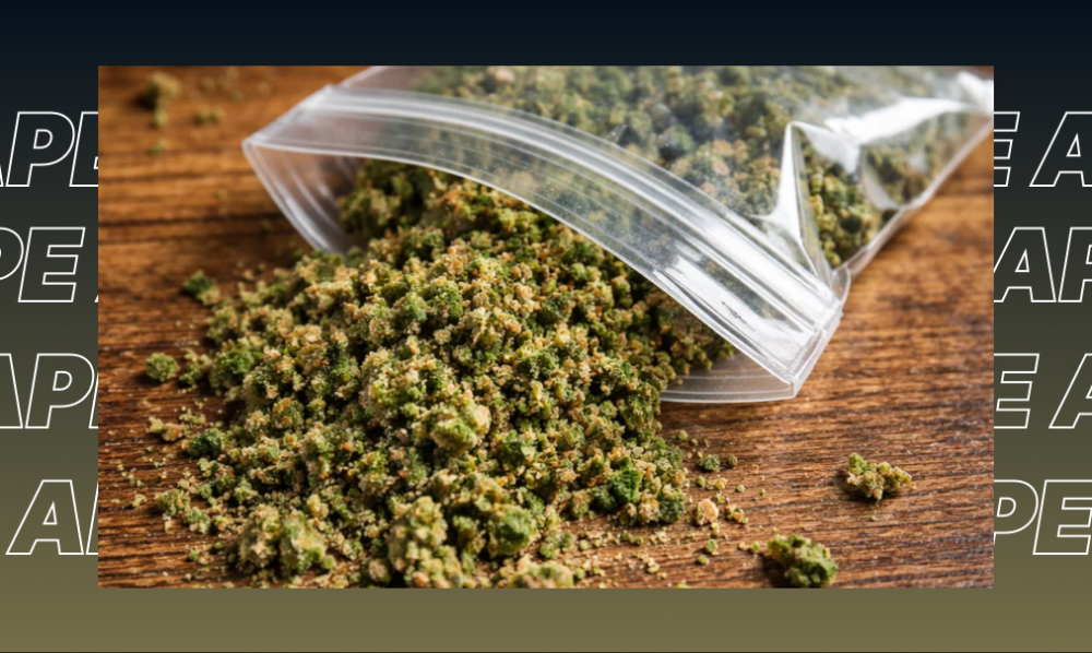 Close-up of ground green cannabis flower spilling out of a clear plastic bag on a wooden surface.