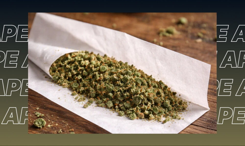 Finely ground green cannabis flower spread across a white rolling paper on a rustic wooden surface.