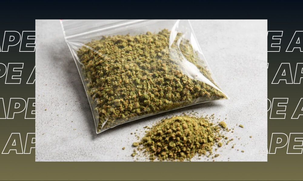 A small plastic bag filled with ground-up green cannabis flower next to a small pile of loose herb on a grey surface.